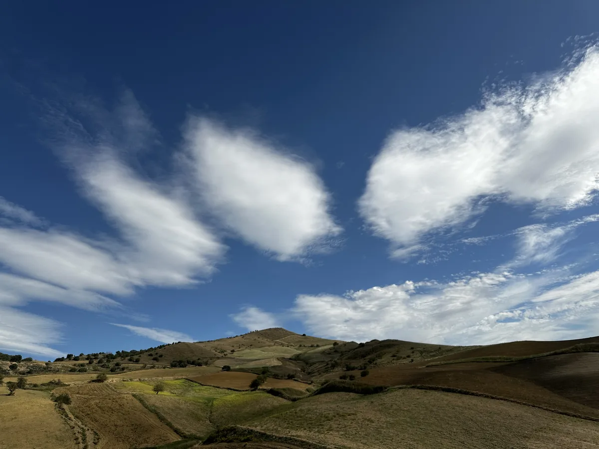 Fotografie: Hügellandschaft unter Zirruswolken vor tiefblauem Himmel
